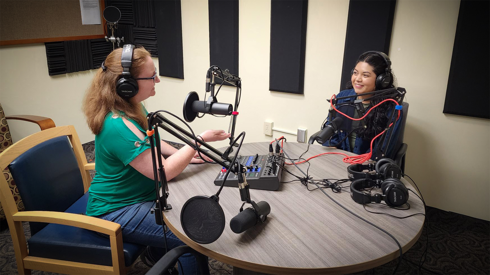 Two women recording in a podcast studio in front of microphones